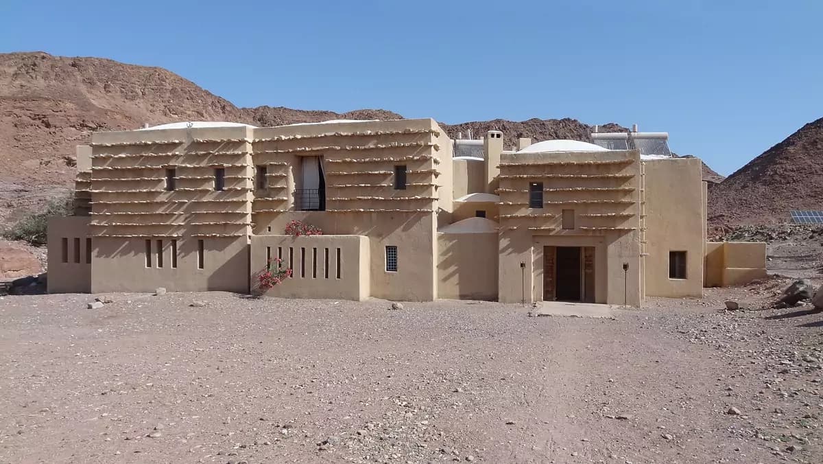 Earth-walled eco-lodge with wooden slats shading its walls in a desert valley