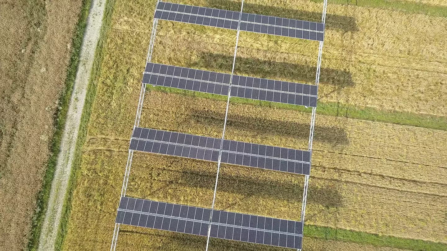 Aerial view of solar panels raised on stilts above a farm field